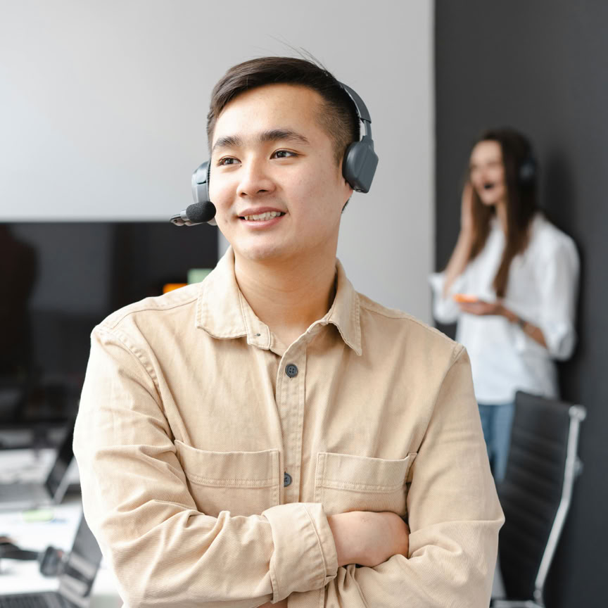 Smiling call center operator in a modern office with arms crossed, wearing a headset.