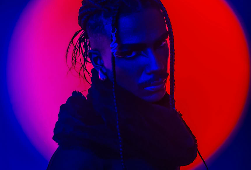 A person with braids in dramatic red and blue light creating a vivid, captivating image.